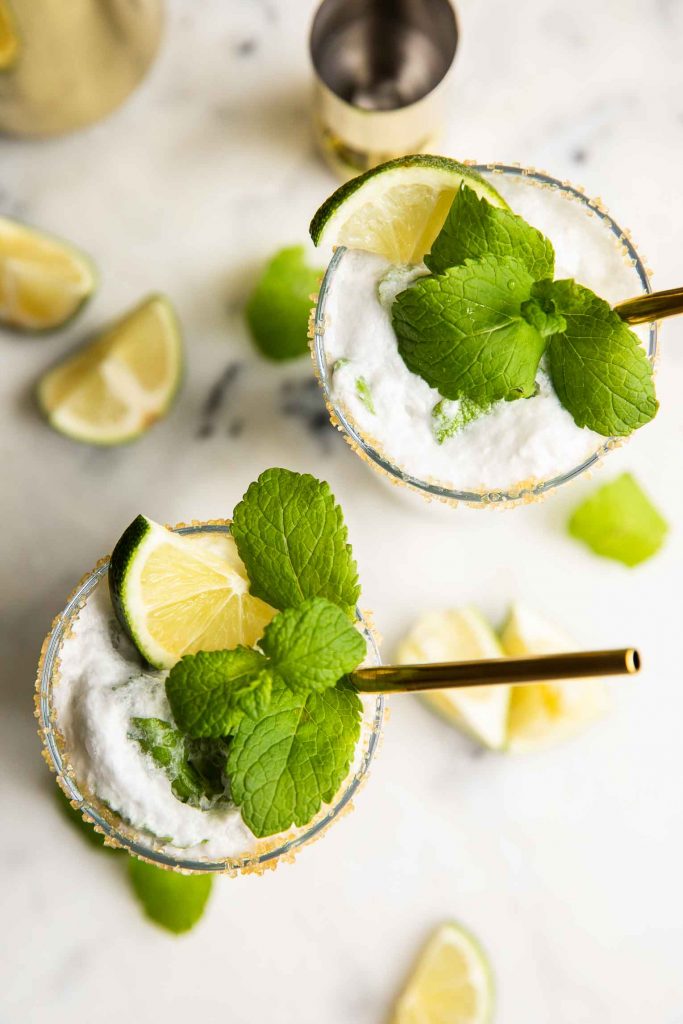 Top shot of coconut rum mojitos with gold straws, lime, and mint.