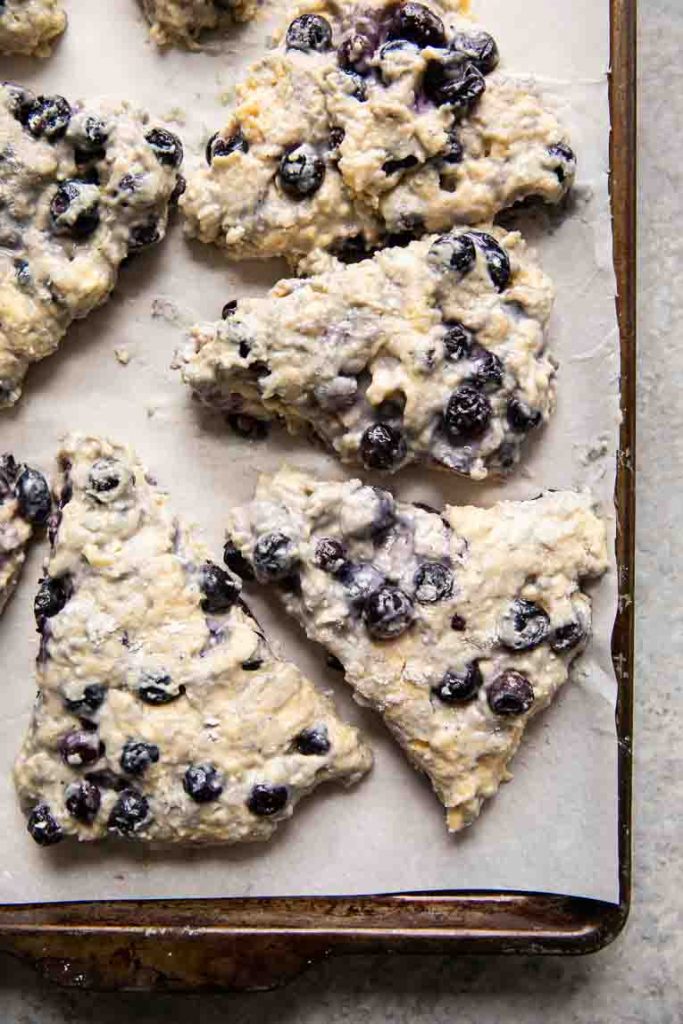 Raw blueberry scones on a baking sheet.