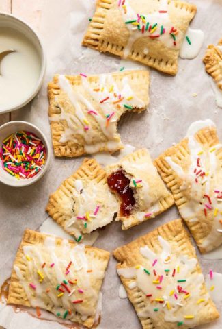 Strawberry pop tarts on parchment paper with icing and sprinkles.