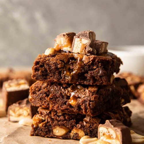 The best ever snickers brownies stacked with pieces of snickers on top.