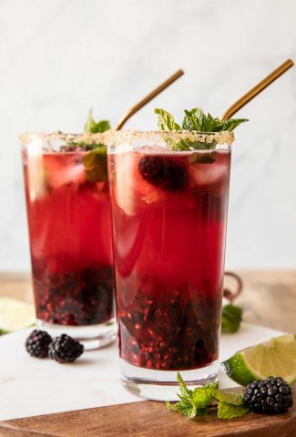 Close up of two blackberry mint mojitos garnished with sugar rim and mint.