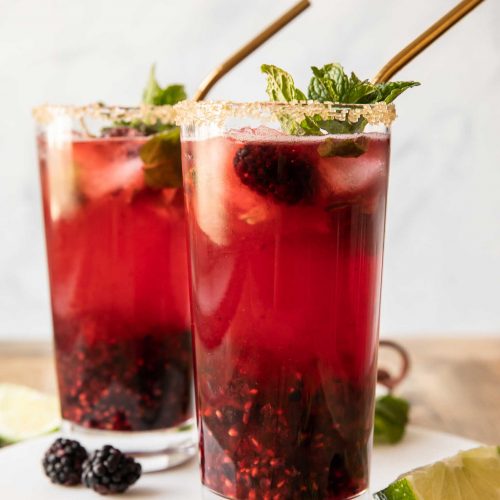Close up of two blackberry mint mojitos garnished with sugar rim and mint.
