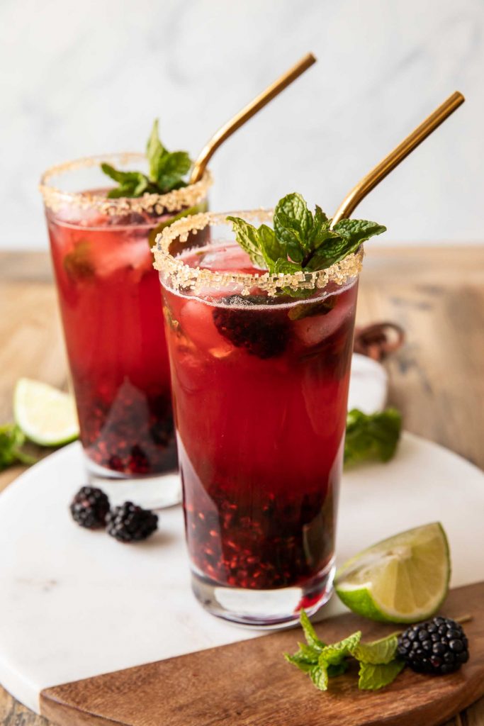 Blackberry mojitos on a wood table with lime and mint.