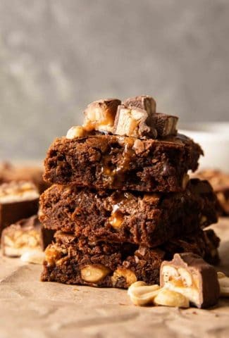 The best ever snickers brownies stacked with pieces of snickers on top.