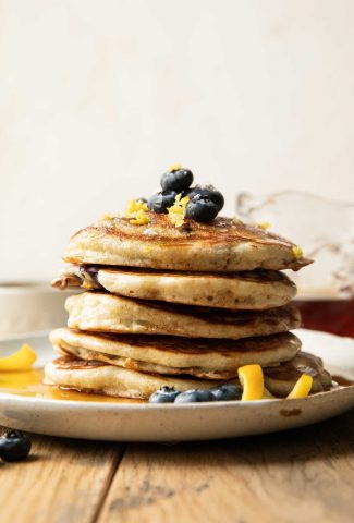 Stack of lemon blueberry pancakes with fresh berries and lemon zest.