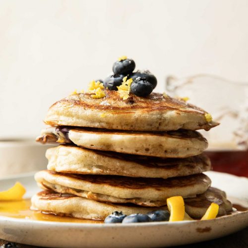 Stack of lemon blueberry pancakes with fresh berries and lemon zest.