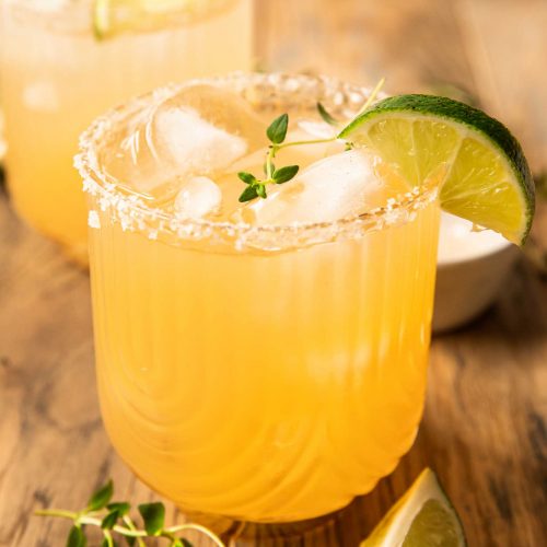 The BEST Rum Margarita recipe with ice, thyme, and a lime wedge.