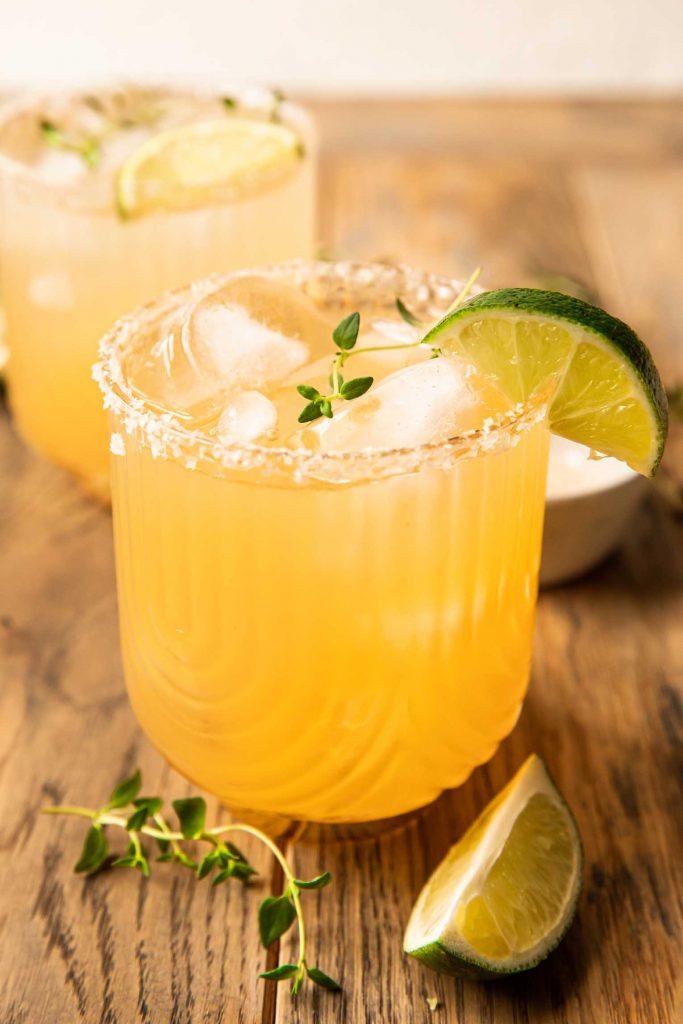 The BEST Rum Margarita recipe with ice, thyme, and a lime wedge.