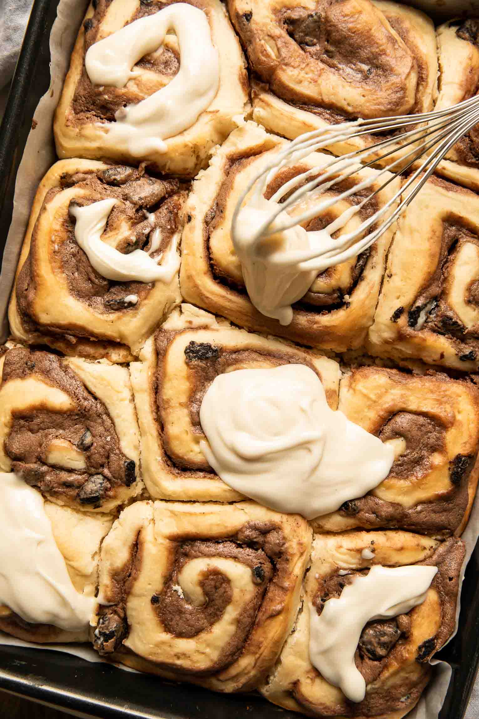 Icing being poured on cinnamon rolls.