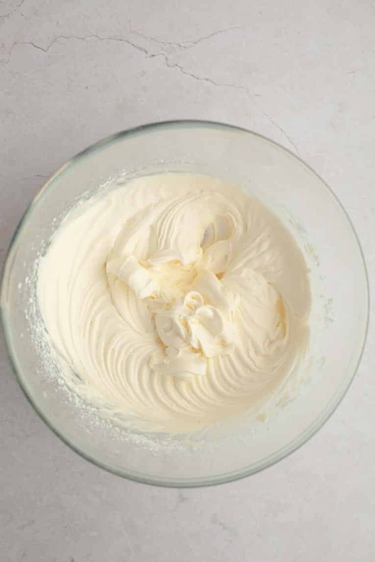 Cream cheese frosting being mixed together in a glass bowl.