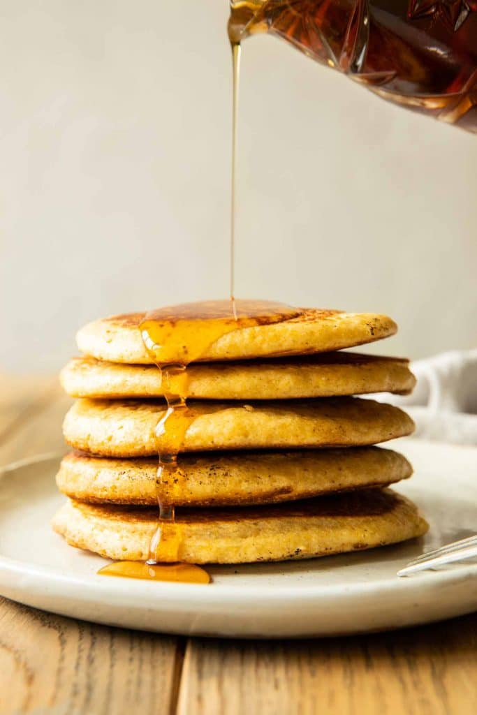 Syrup pouring on to a stack of cornbread pancakes.