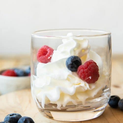 Mascarpone Whipped Cream recipe in a glass cup with berries.
