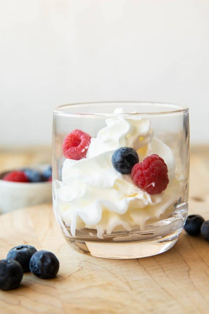 Mascarpone Whipped Cream recipe in a glass cup with berries.