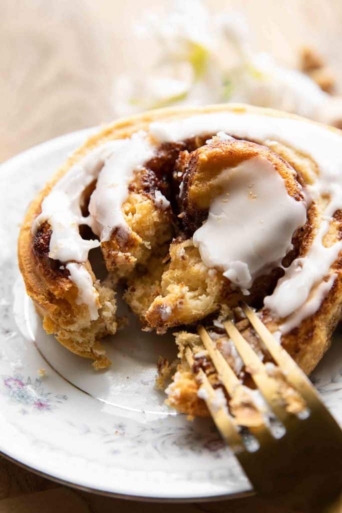 Angled close up of a large, fluffy cinnamon roll with a bite taken out and a fork.