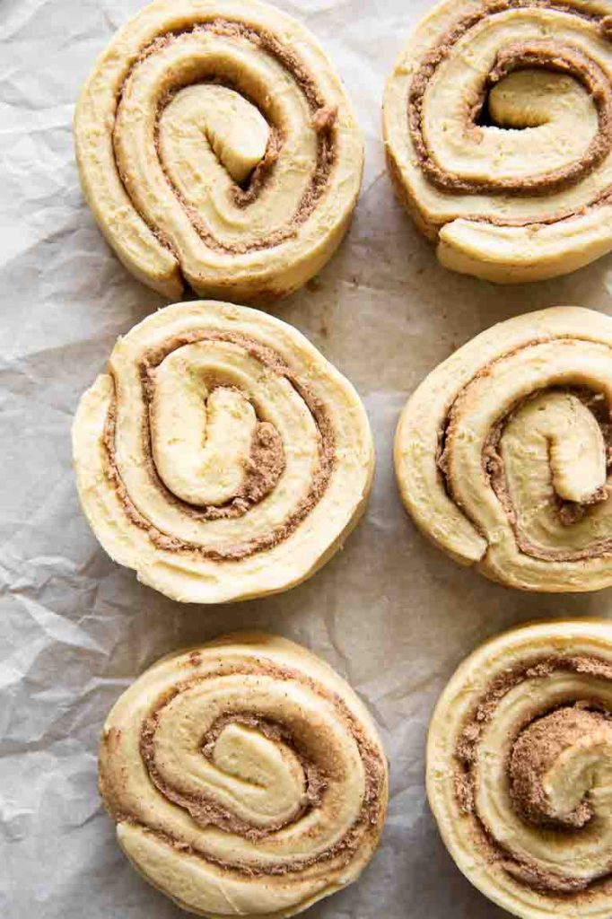 Raw cinnamon roll dough with filling on a baking sheet.