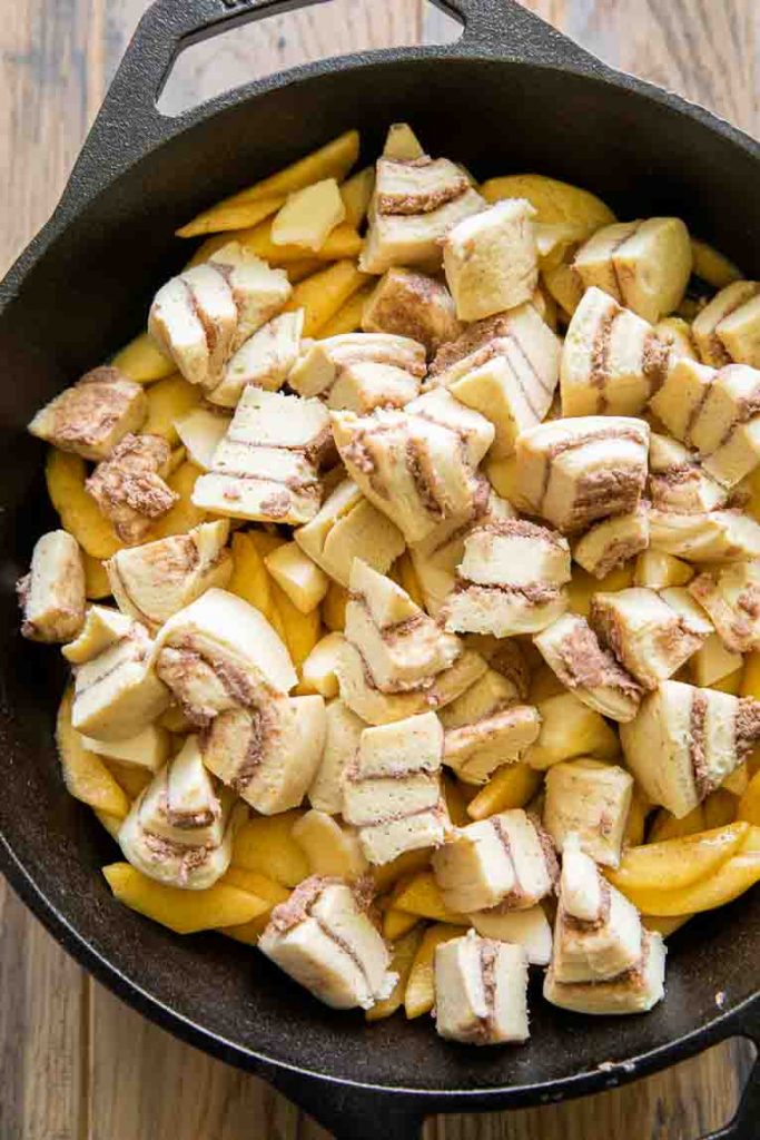 Peach pie filling with cinnamon roll pieces in a skillet.