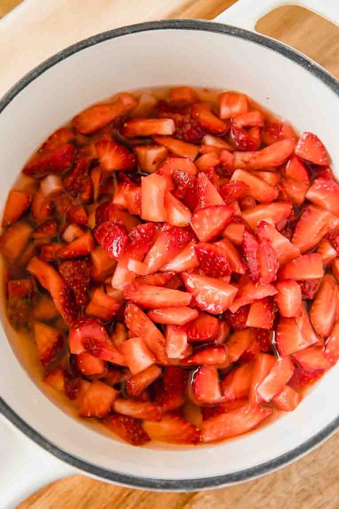 Strawberries in a pot being mixed with sugar.