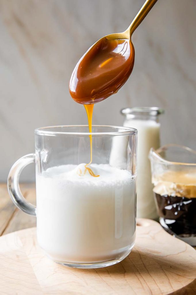 Caramel sauce being poured into frothy steamed milk.