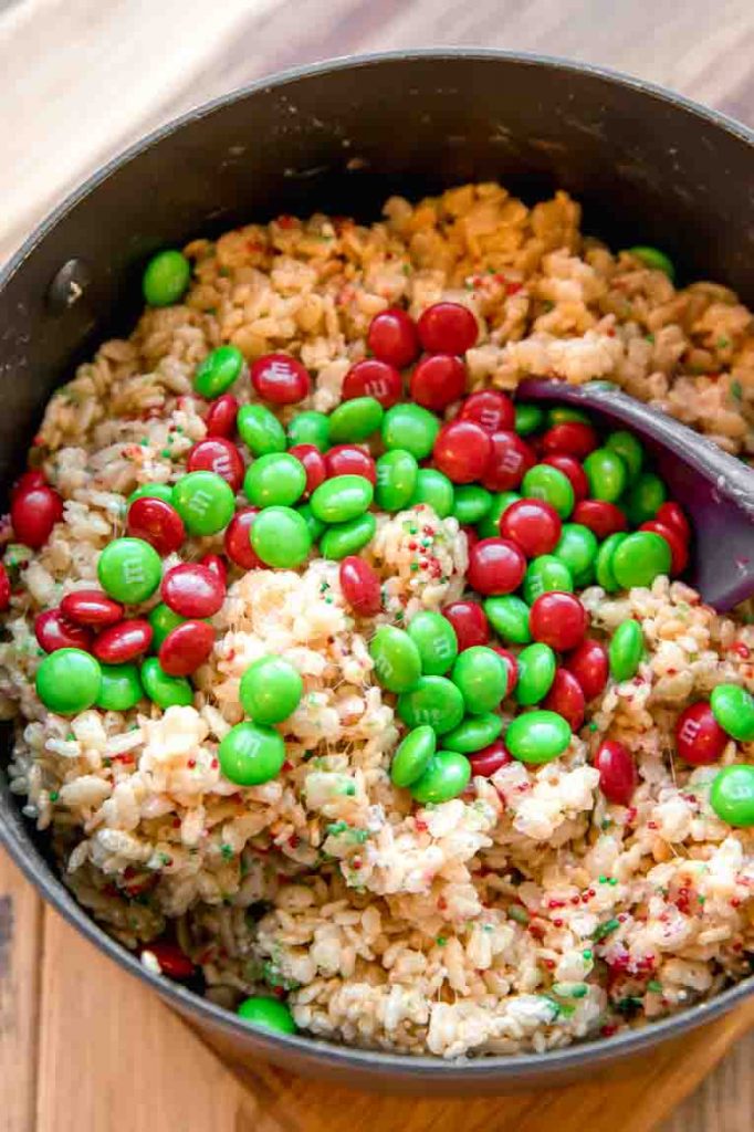 Red and green M&Ms mixed into rice krispy treats in a pot.