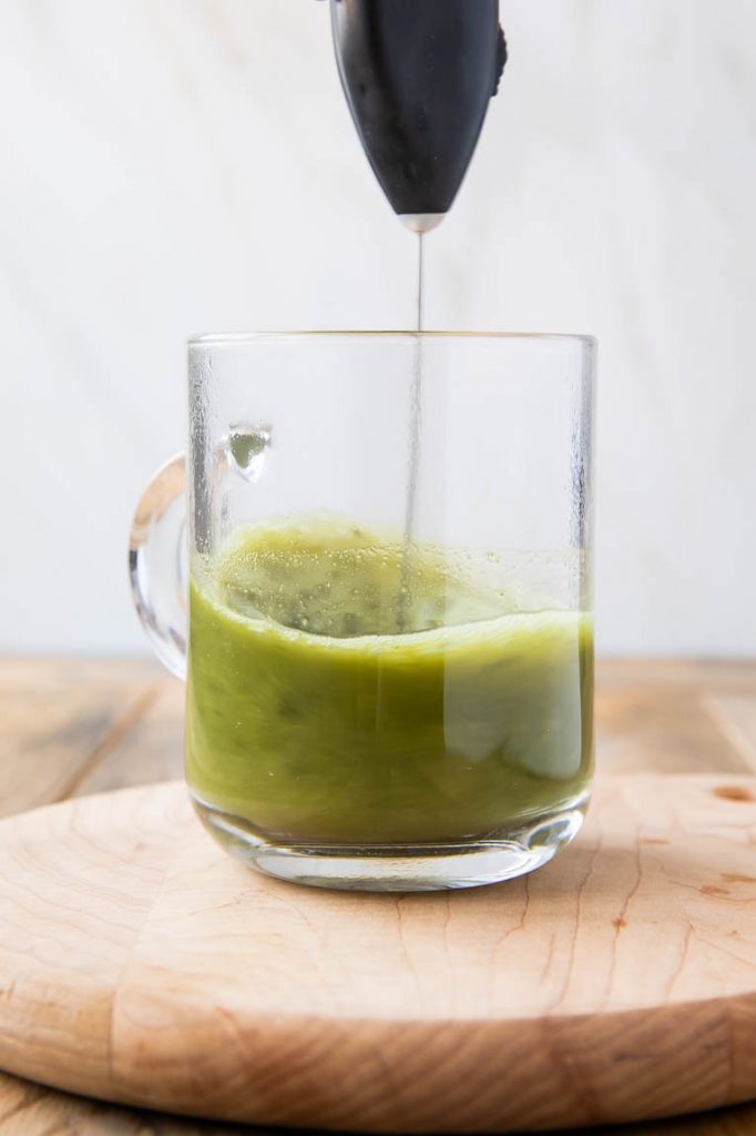 Matcha and hot water being whisked together.