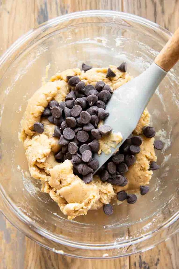 Cookie dough with chocolate chips being mixed in a mixing bowl.