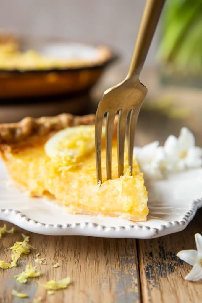 Lemon chess pie slice with a fork taking a bite.
