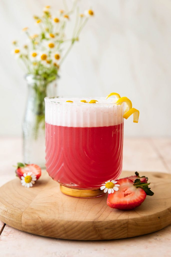 Pink Gin Sour cocktail with flowers and strawberries.