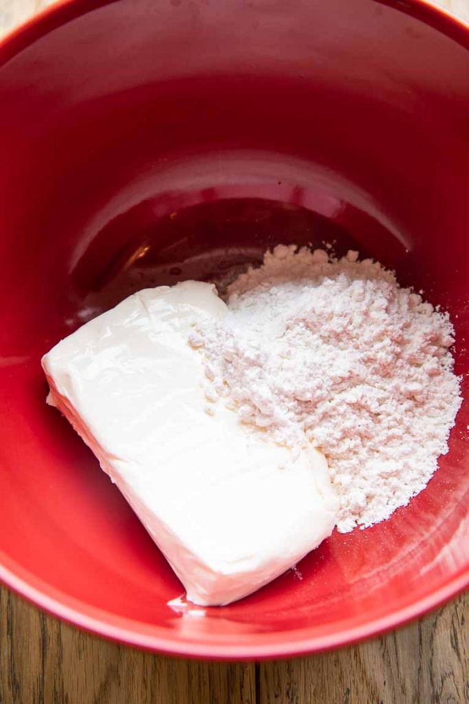 Cream cheese and powdered sugar in a mixing bowl for no-bake cheesecake.