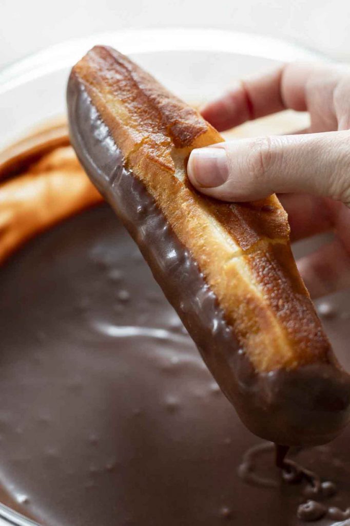 Long John Donuts being dipped in a chocolate glaze.
