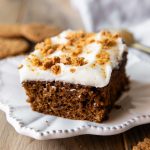 Slice of gingerbread cake with icing and crumbled cookies on top.