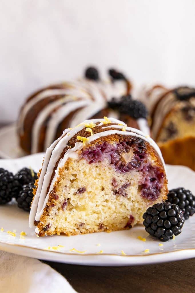 A slice of lemon blackberry cake on a cake stand.