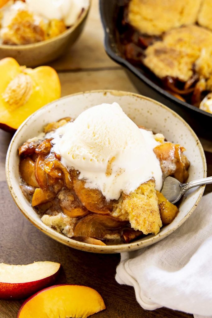Peach cobbler in a bowl with ice cream.