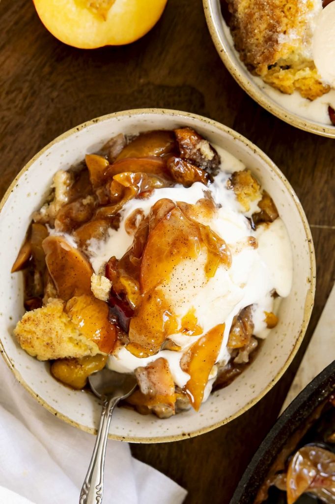Peach cobbler in a bowl with ice cream.